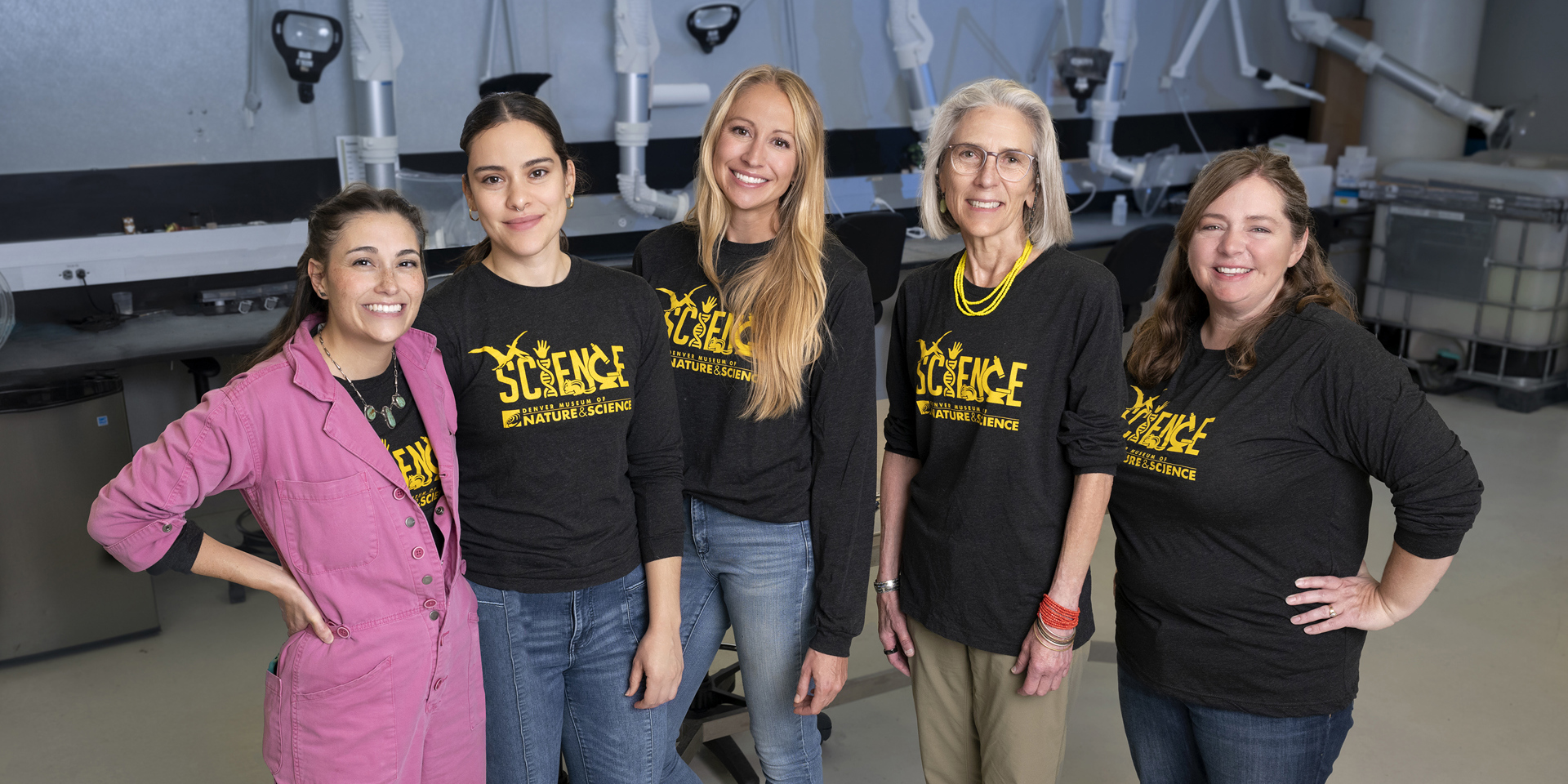 Five women in black Science shirts stand in a line in a lab