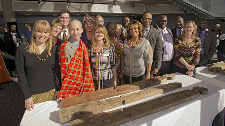 Large group of Museum staff and Kenyan representatives pose near vigango