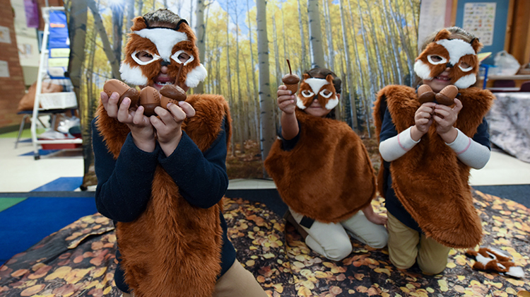 Three children dressed in chipmunk masks present their acorn findings to the camera