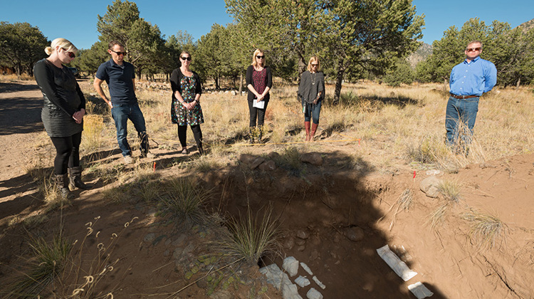 Six individuals stand near an open grave during a moment of silence