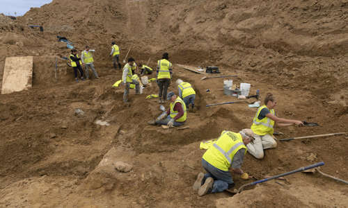 a wide view of a large excavated dirt area with a group of people working in it.