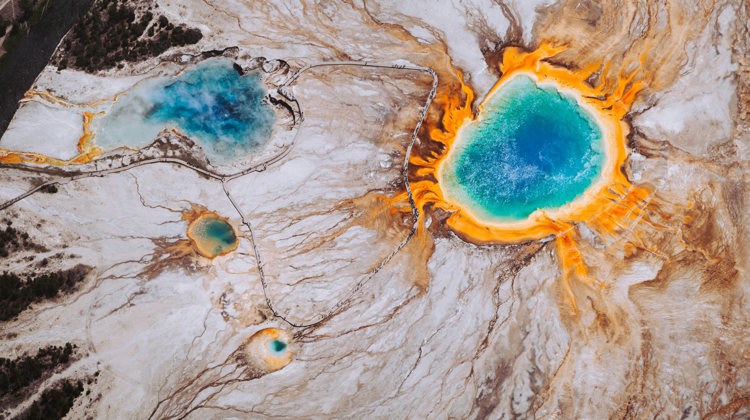 A drone image shows Yellowstone National Park from above with its vibrant blue and orange hot pools.