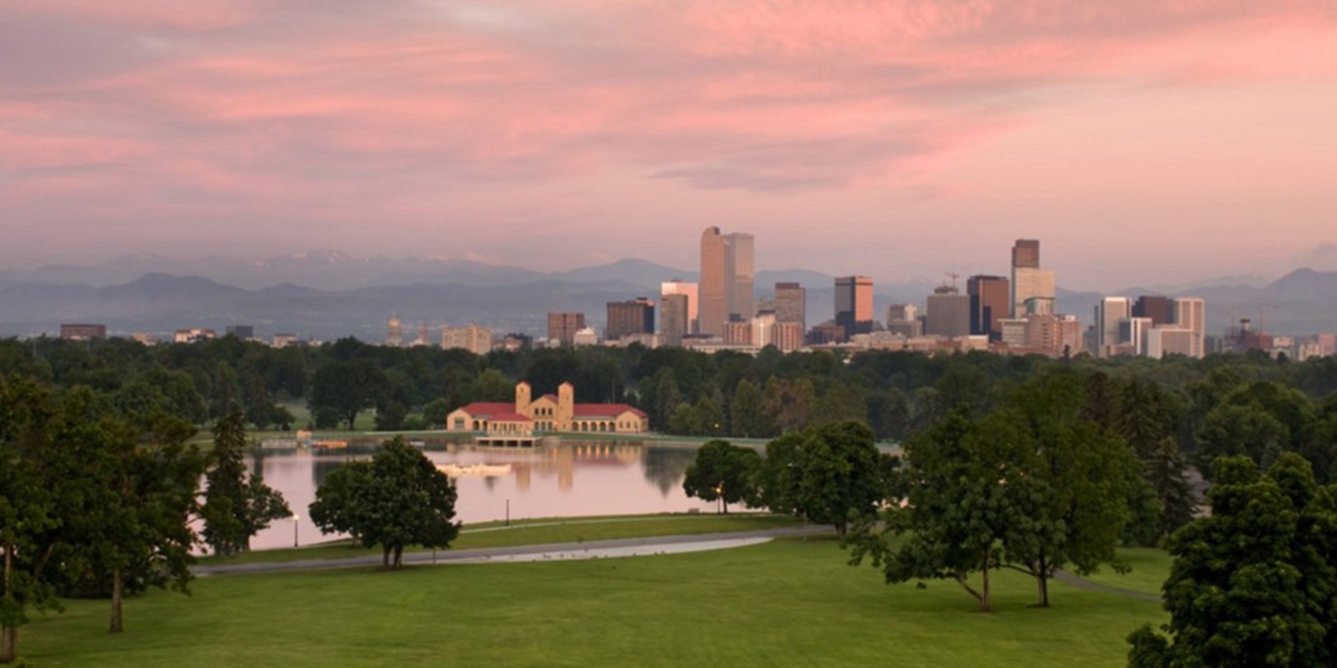 A view of City Park and Downtown Denver including a lake, the skyline, and mountains at sunset