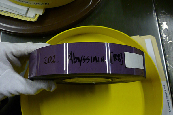 a white-gloved hand holding an old film reel with the label "abyssinia"