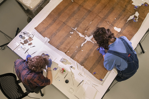 Overhead view of two staff working to conserve a damaged textile