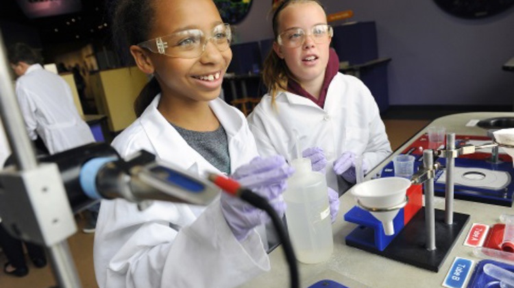 Two students exploring wearing white lab coats and purple gloves complete a science experiment in Expedition Health