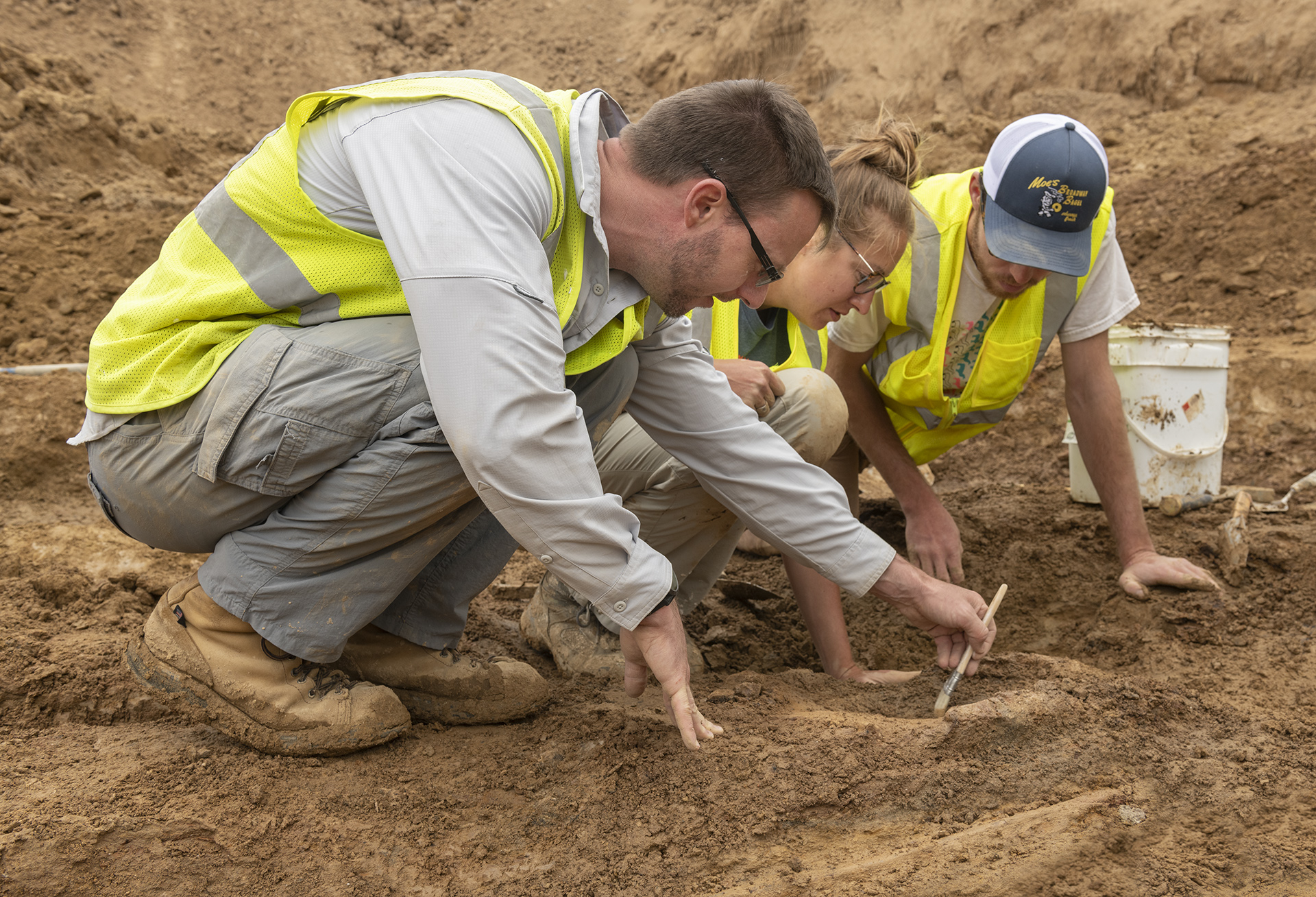 Three people using tools to excavate a paleontological site