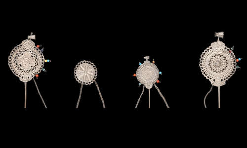 Four ornate silver pins arranged on a black background