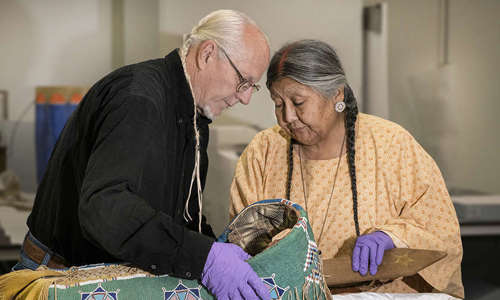 Two elders examine a cradleboard